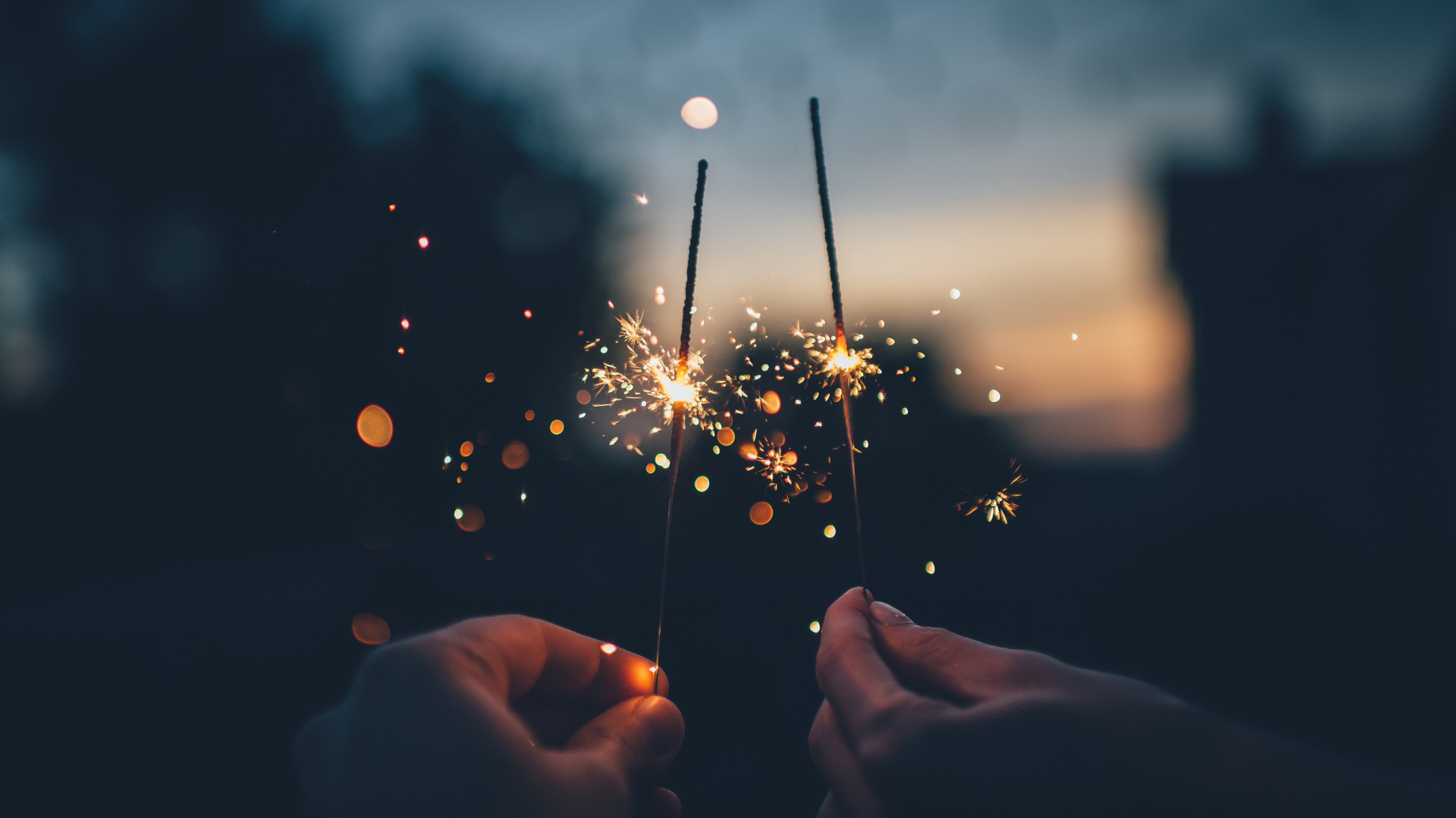 Two people hold sparklers at dusk