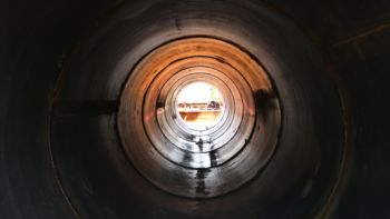 A view down the inside of a large pipe. There is light at the end of the pipe.