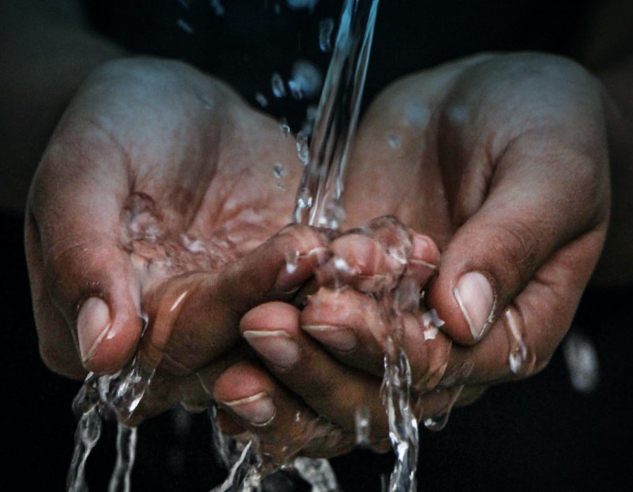 A pair of cupped hands catching clear water being poured from above