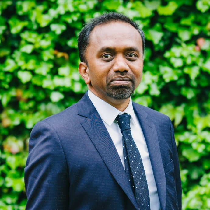 Fredrick Royan stands in front of an ivy hedge and smiles at the camera
